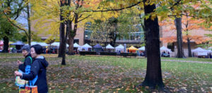 photo of two shoppers at a farmers market with canopies in the distance